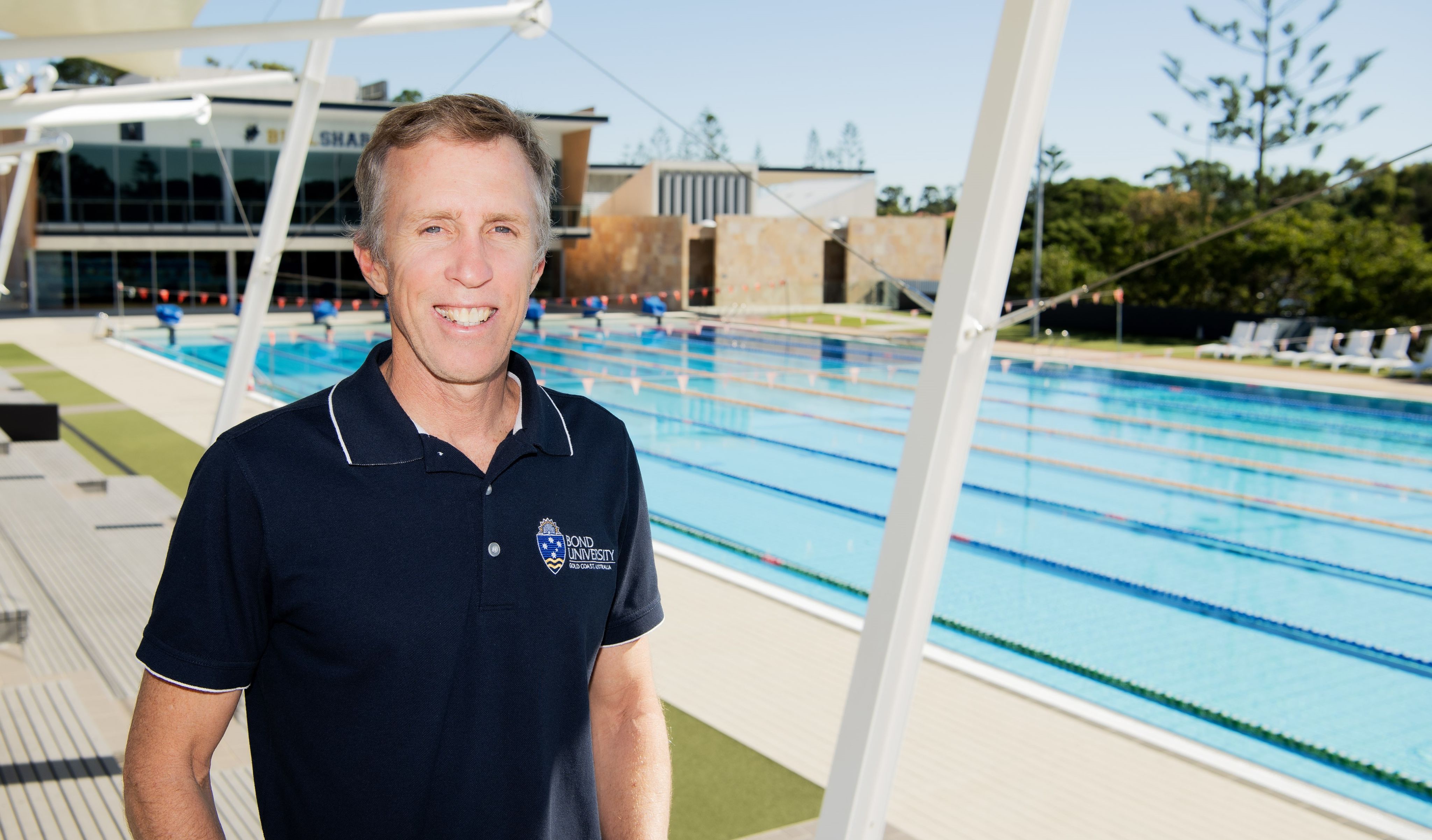 A man is smiling, standing next to a pool.