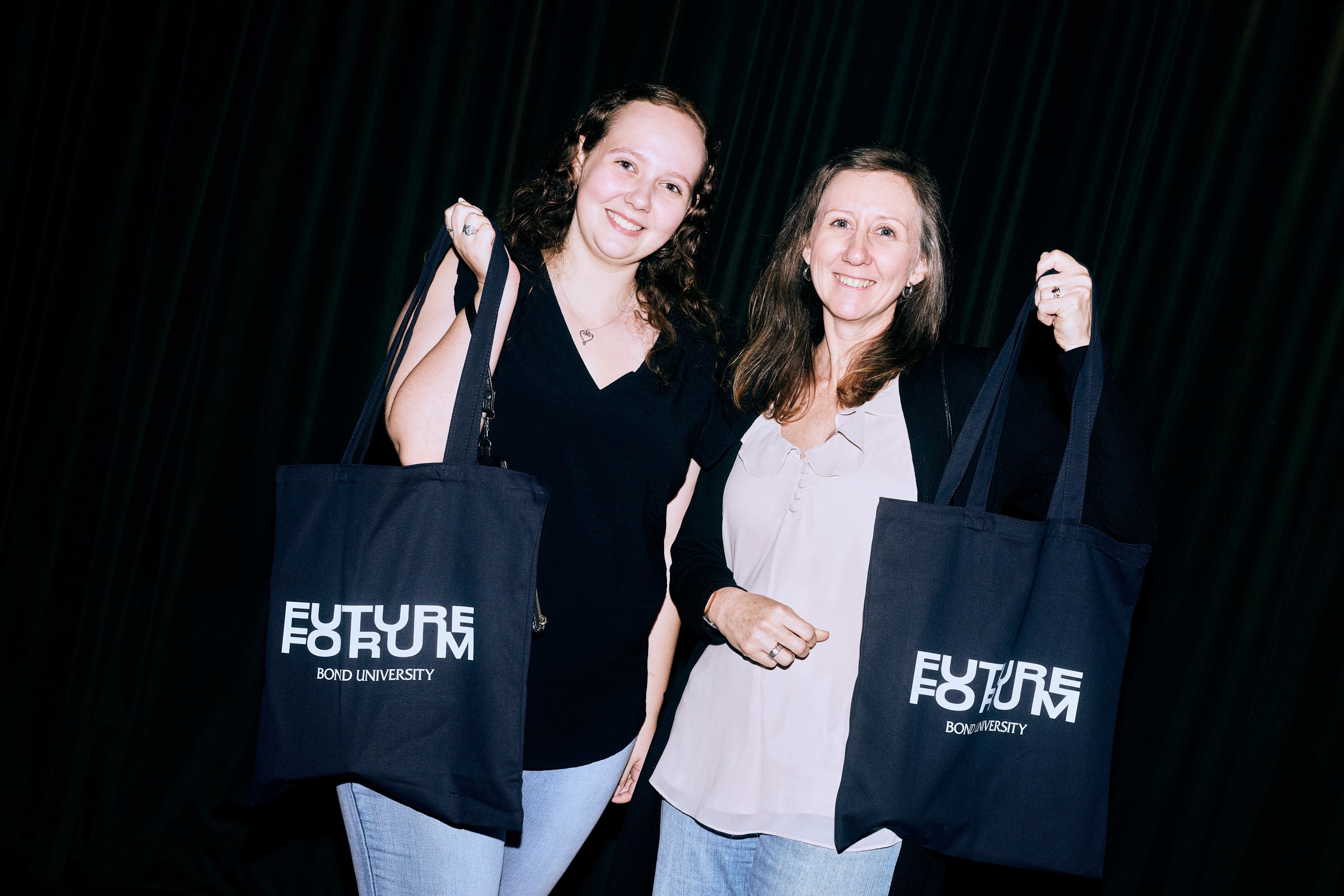 Two people are holding tote bags and smiling