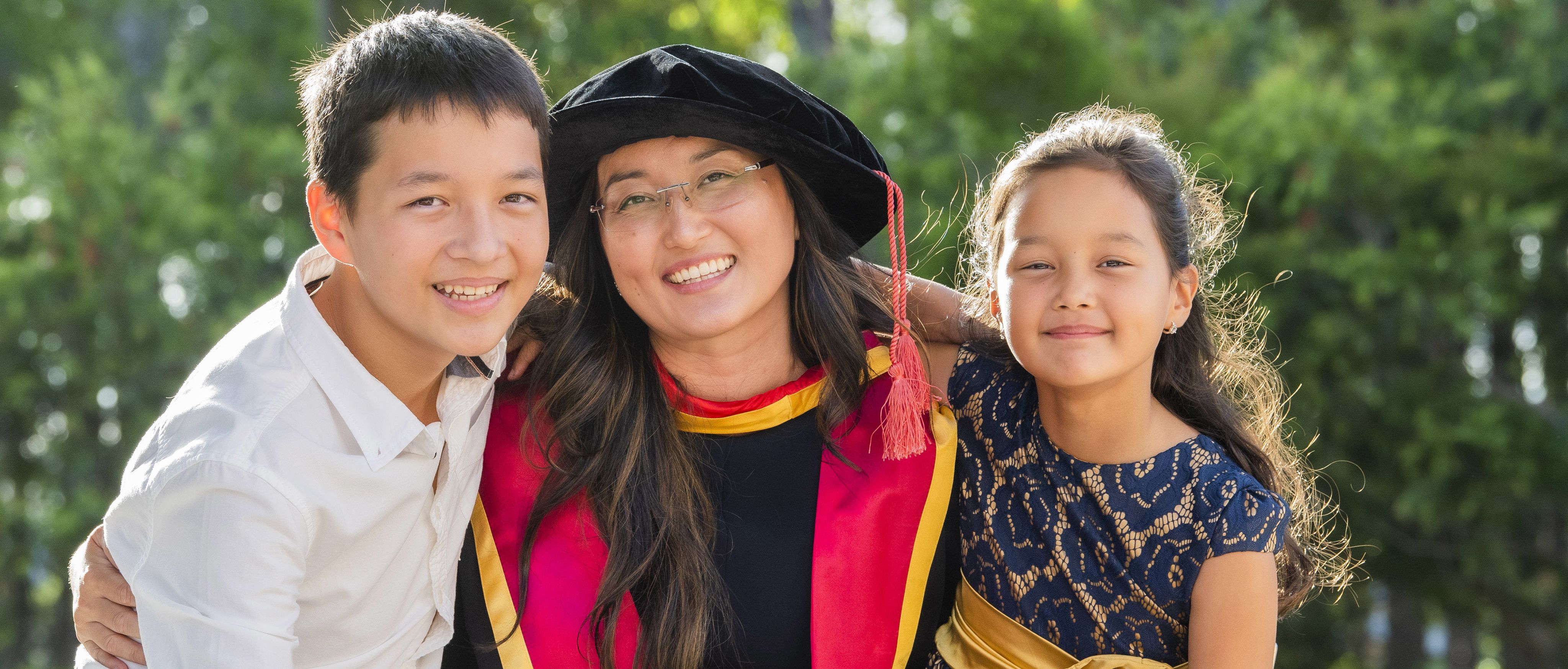 A woman is wearing a graduation hat and smiling alongside two children. 
