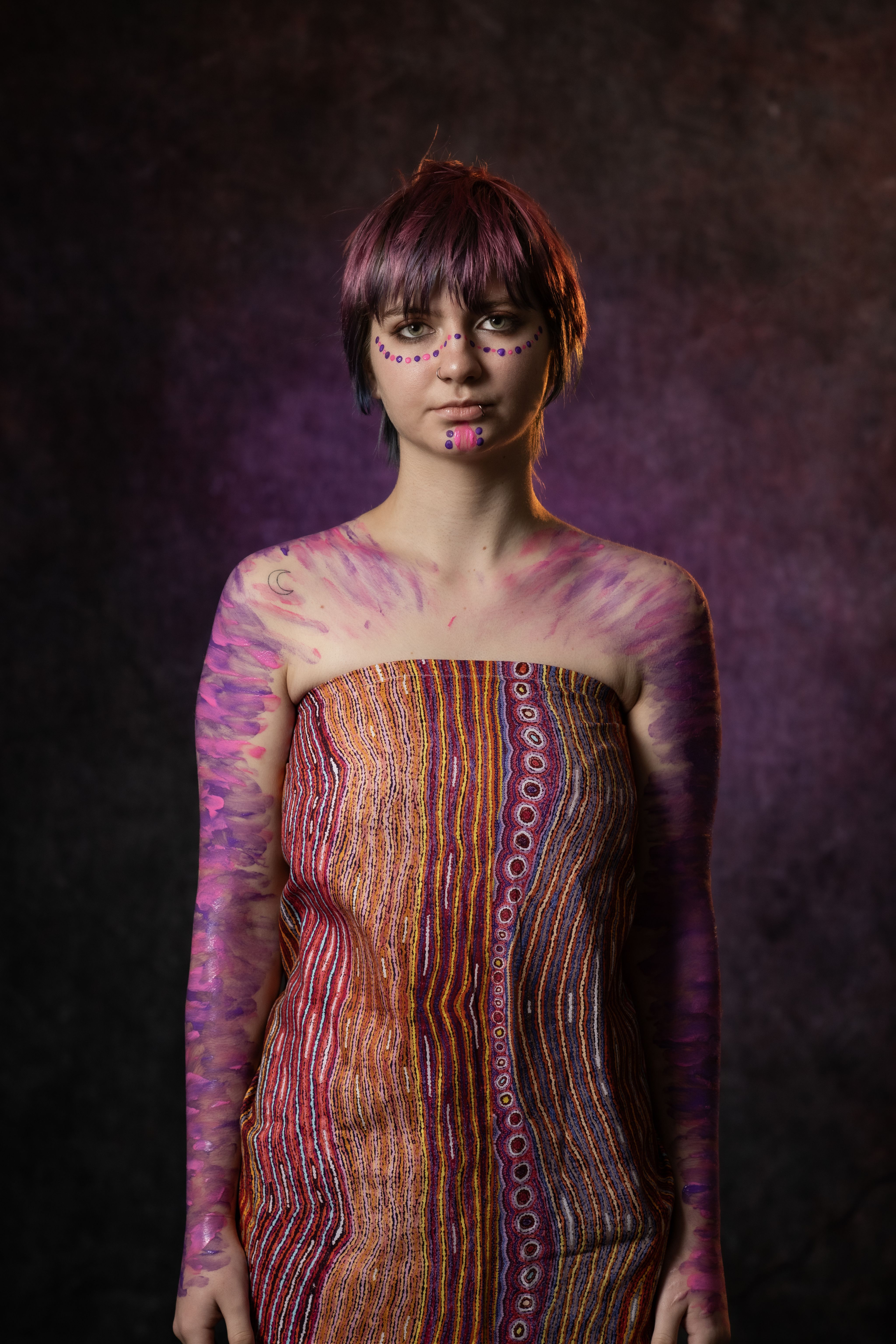 A woman is wearing body paint and a vibrant patterned top.