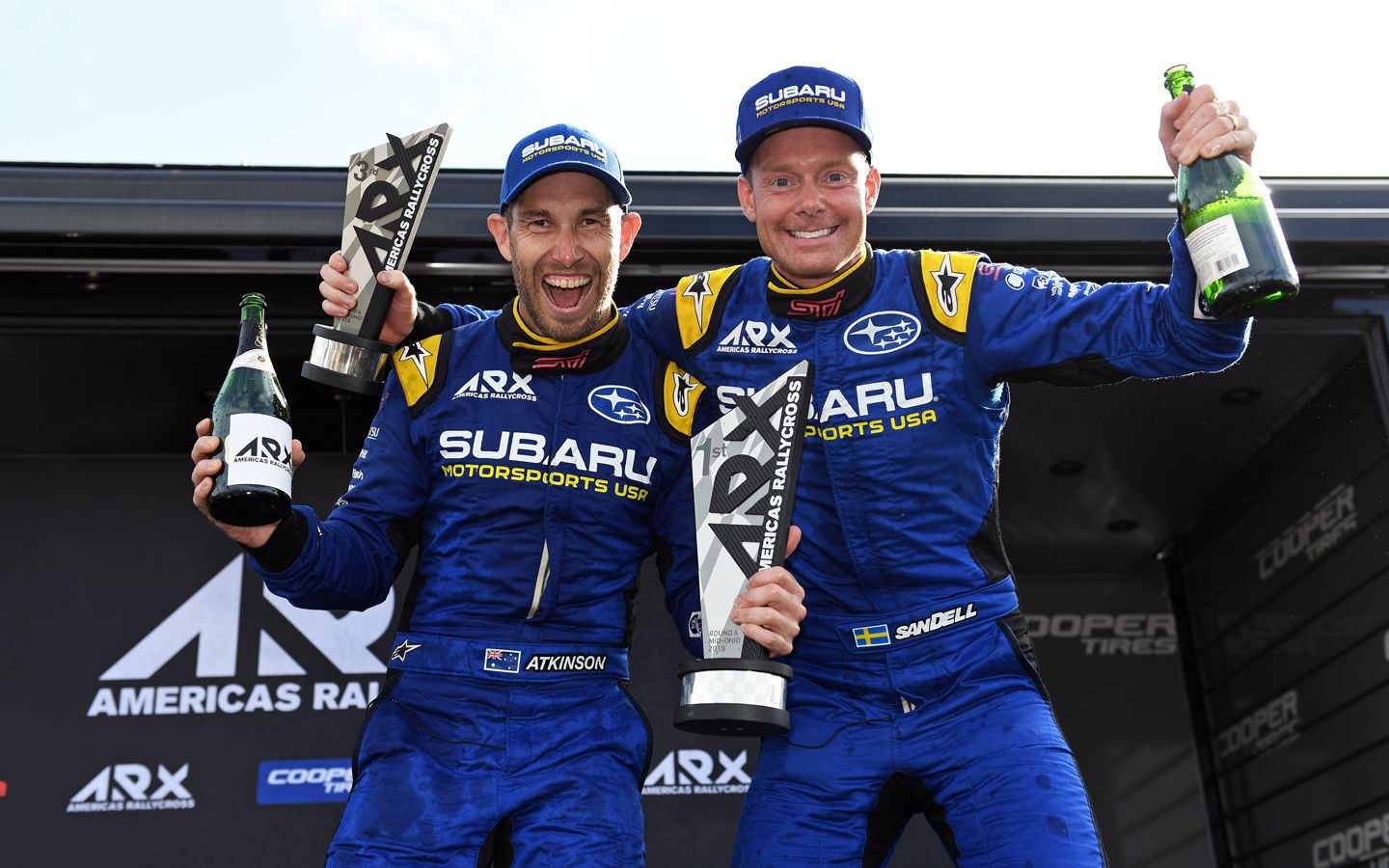 Two men in sports jumpsuits are smiling.