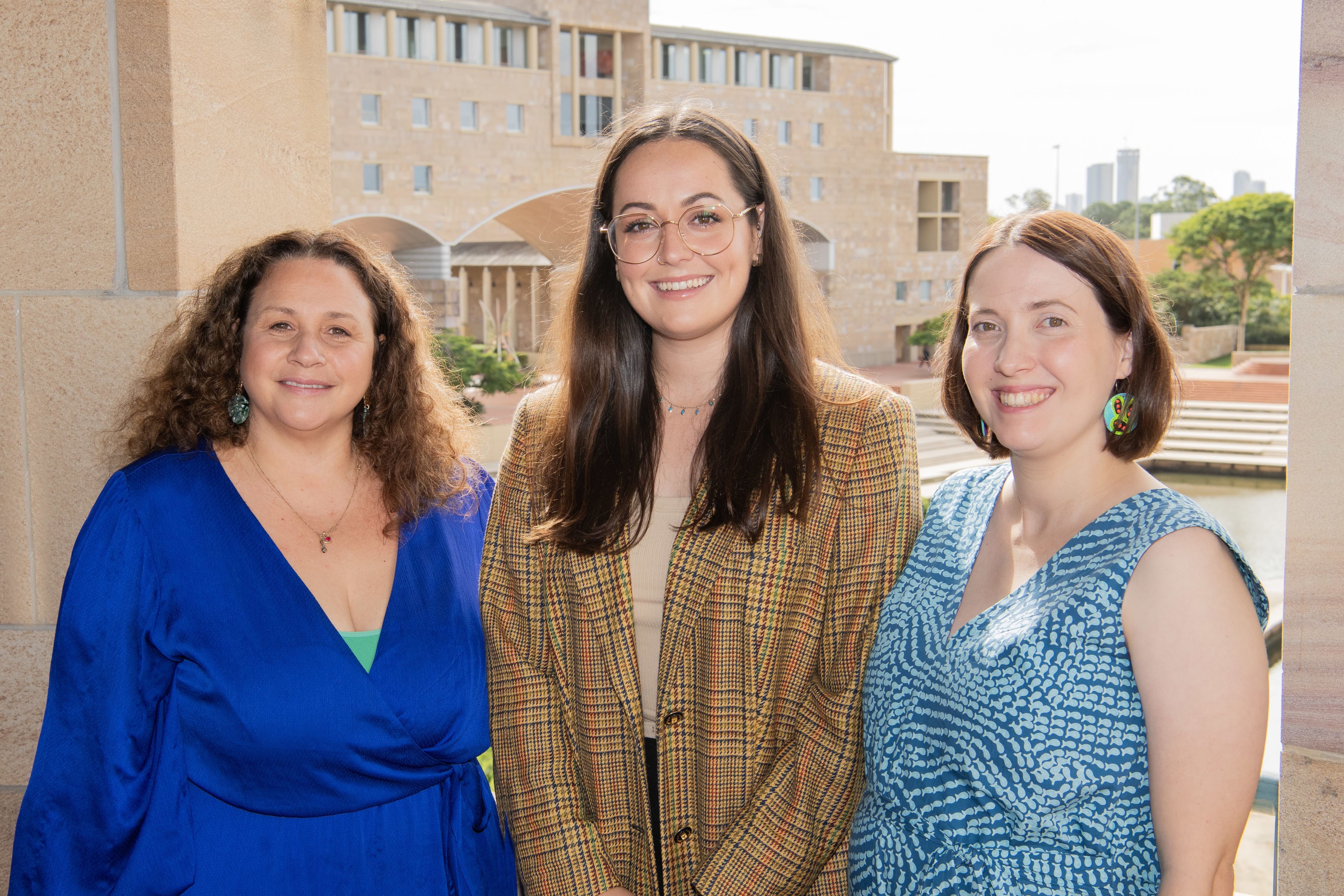 Three women are standing side by side and smiling. 