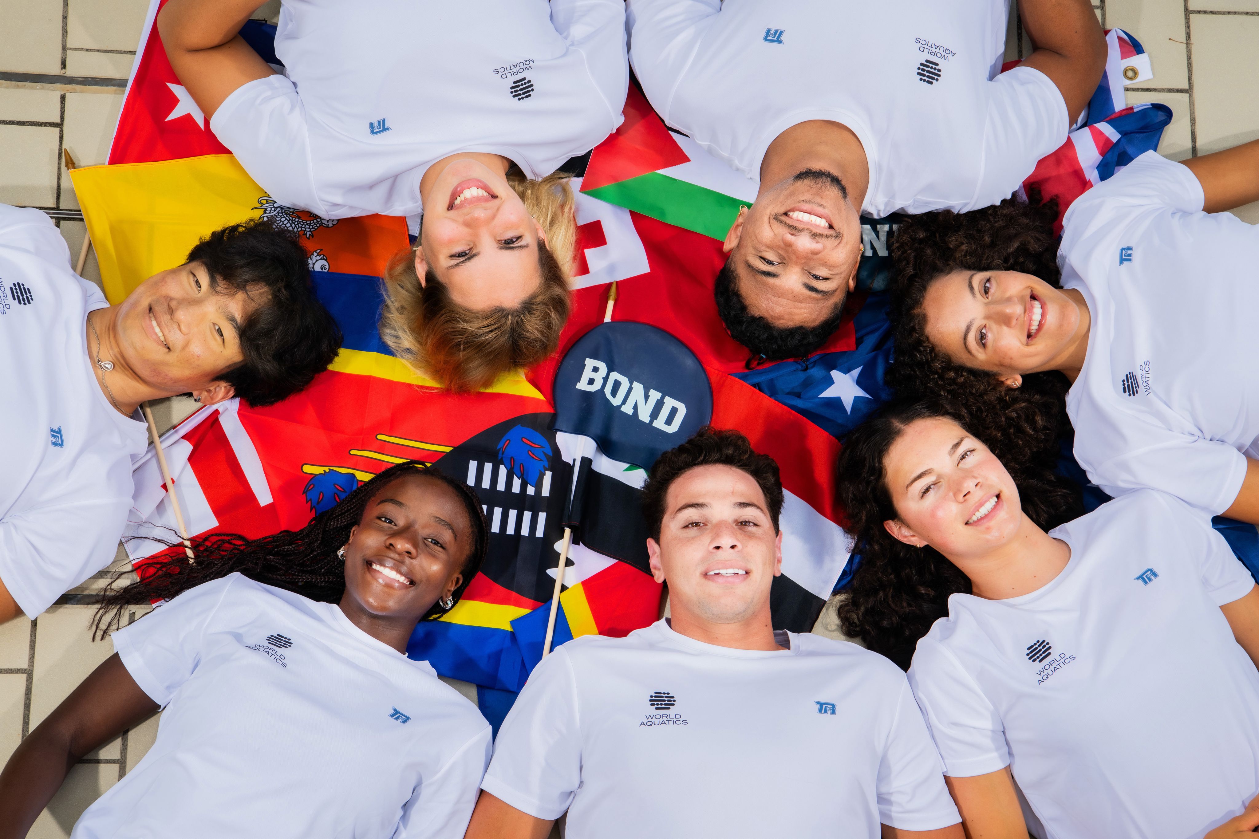 A group of young people are laying with their heads together and various country flags around them