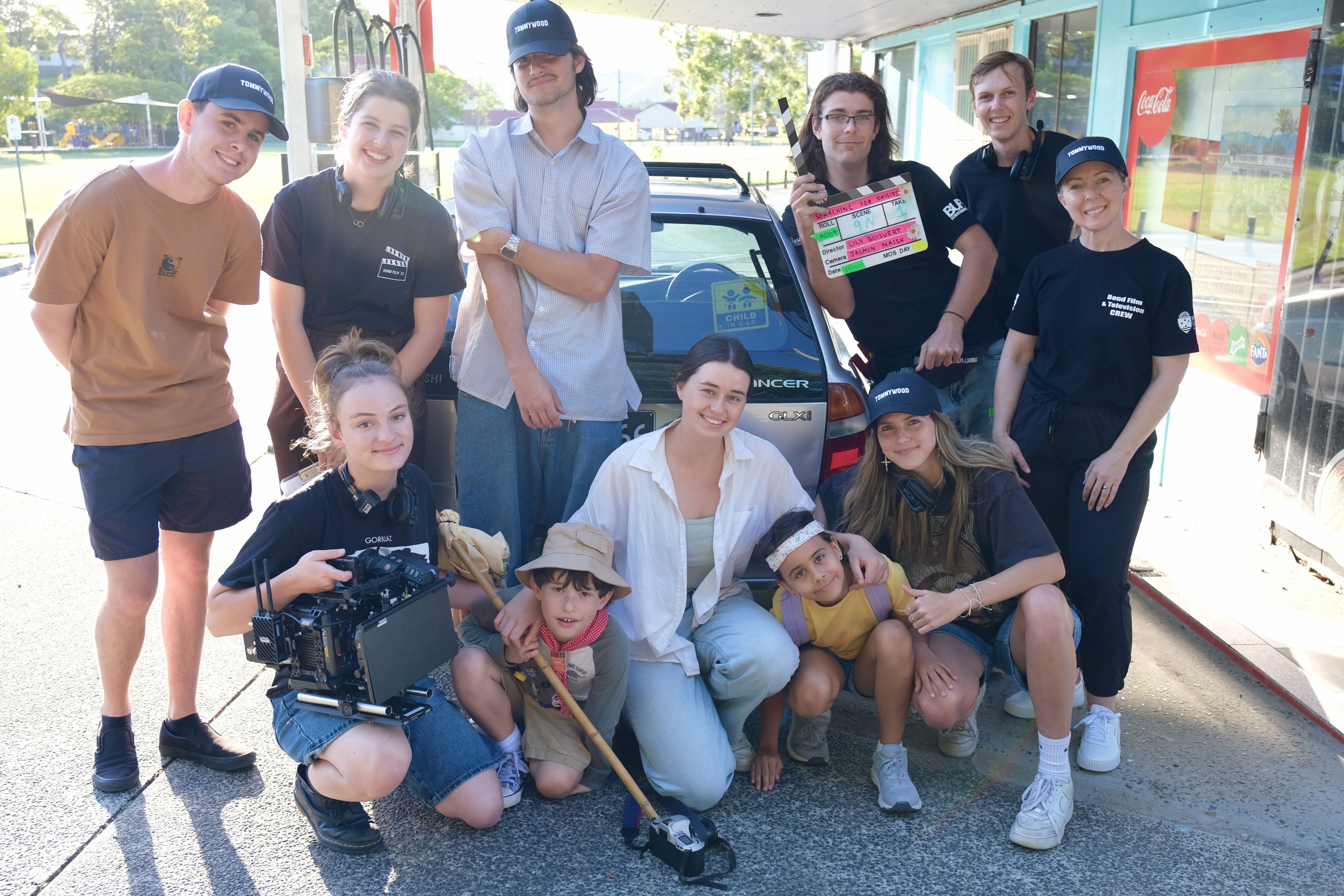 The cast and crew of Searching for Daisies pose for a photo in front of a petrol station