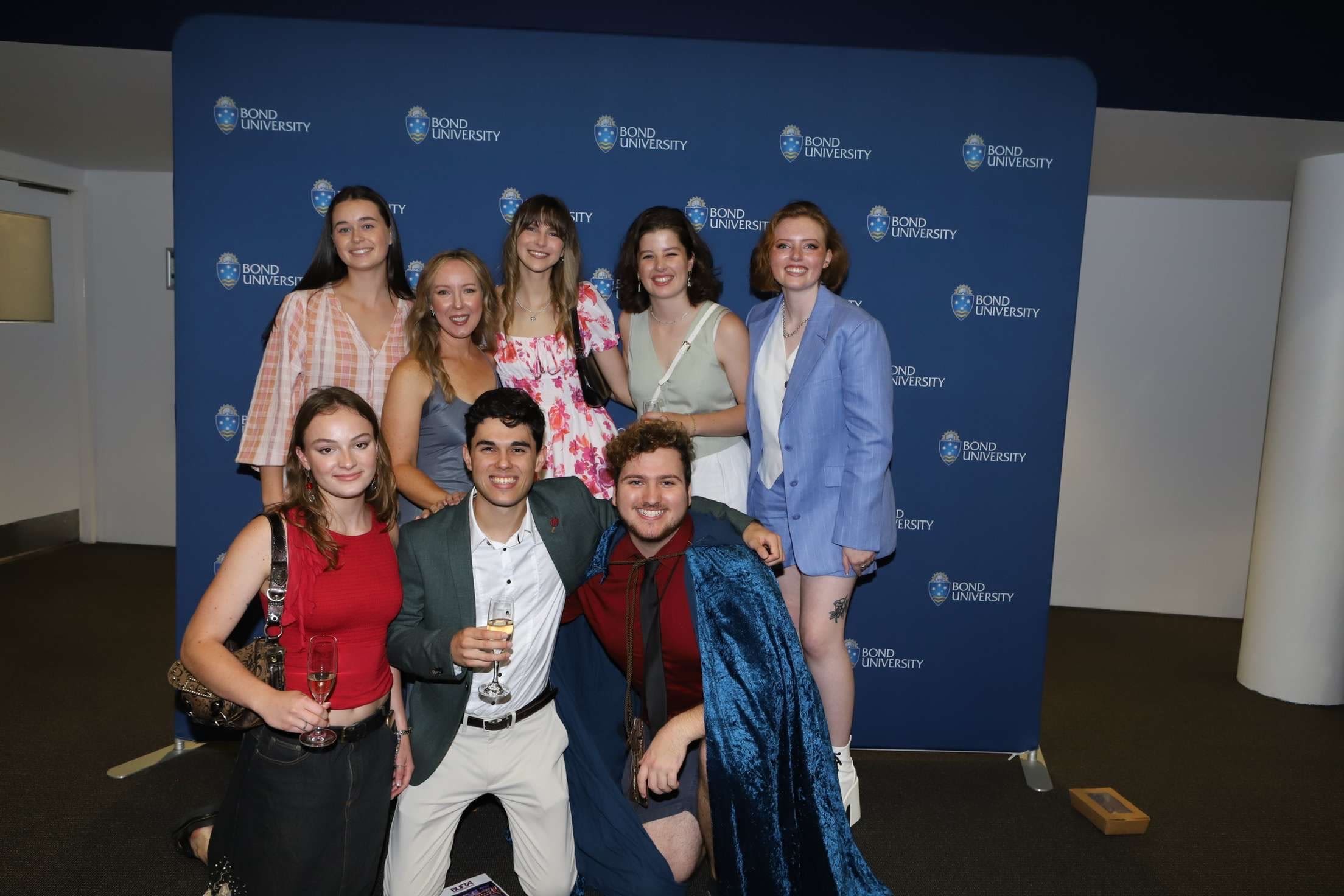 A group of friends pose in front of a media wall 