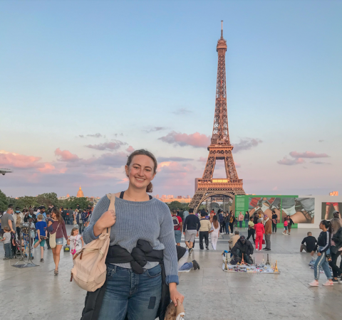 Anna Pata smiles in front of the Eiffel Tower with a sunset in the background