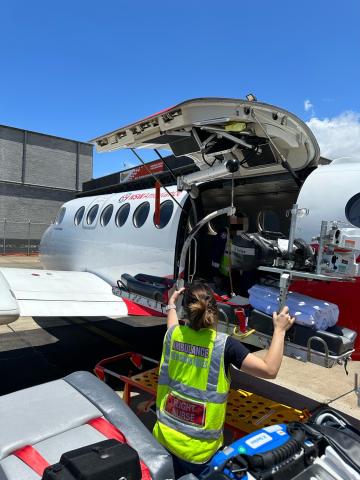 A woman wearing a high-vis vest is loading medical equipment onto a small aircraft. 