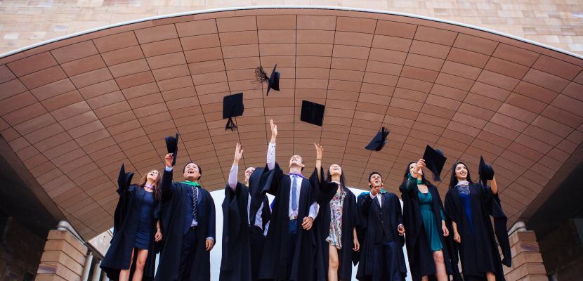Eight Bond University students throwing their mortarboard in the air in celebration of their graduation