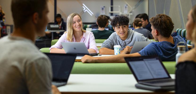 A group of students sitting in the Bond University Library with their laptops on the desk
