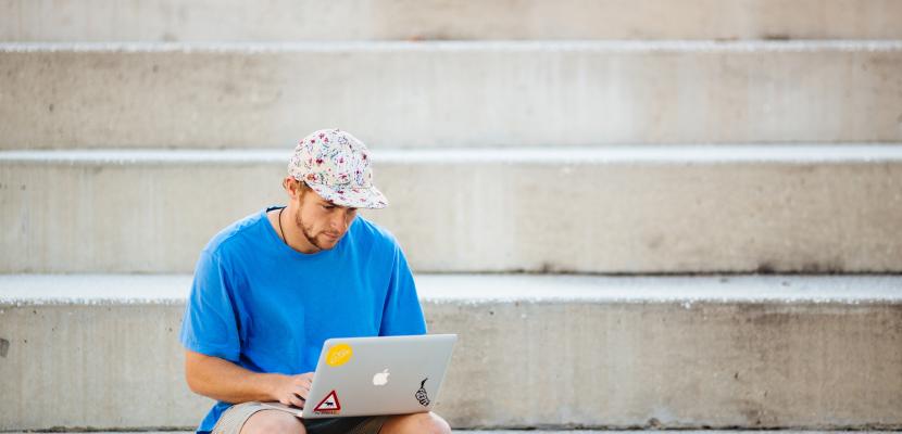 Male student typing on his laptop while sitting on the ADCO Amphitheatre stairs.