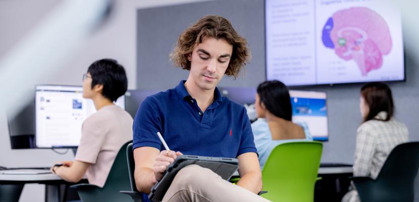 A male student using a tablet and stylus in a Bond University Faculty of Society and Design classroom.