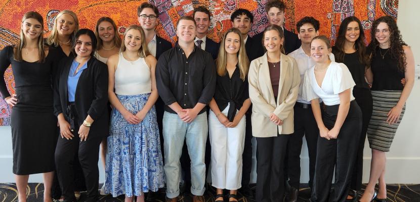 The 2022 student BUSA group stand in front of an indigenous painting smiling at the camera