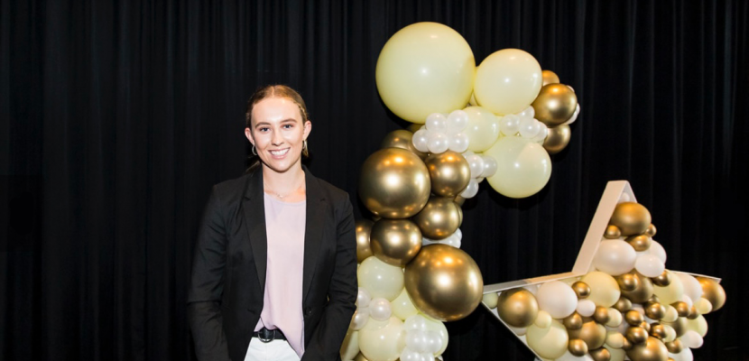 Ella Warrall stands in front of a balloon arch and star made of gold and yellow balloons
