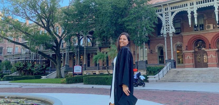 Maju is wearing a graduation cap and gown pictured in front of a building at the University of Tampa
