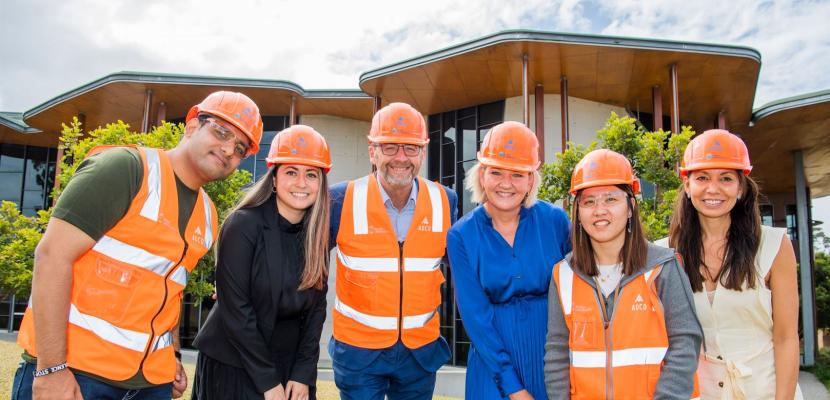 A group of people are wearing high visibility clothing and smiling while standing in front of a building, 