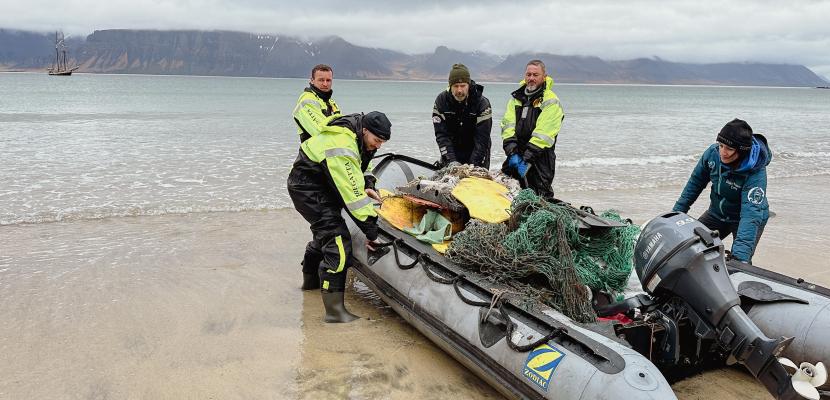 Five people are loading washed up debris onto an inflatable boat.