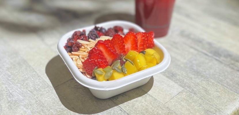 An photo of a smoothie bowl topped with fruit, and a red-coloured juice in a takeaway cup. 