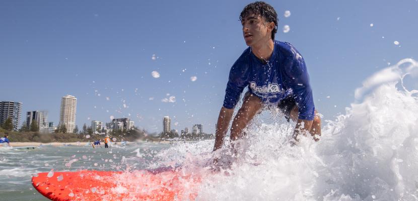 A young man wearing a blue rash shirt is surfing a wave on an orange board.