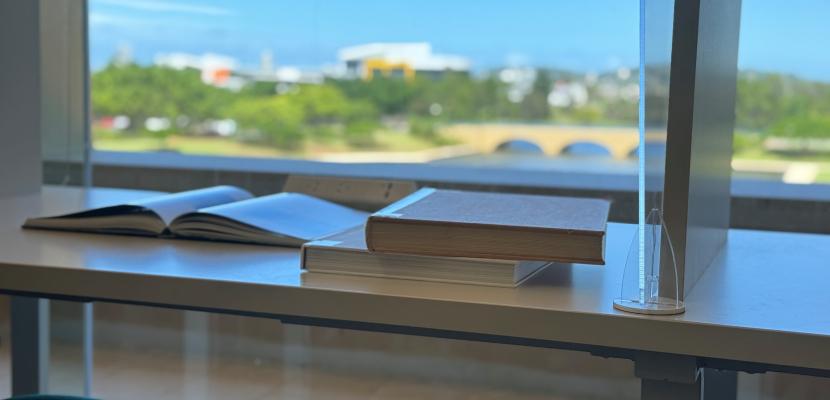 Books are pictured on a desk in front of a window overlooking the lake at Bond University. 