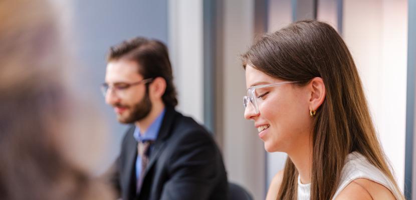 Two students are sitting beside each other, looking down and smiling.