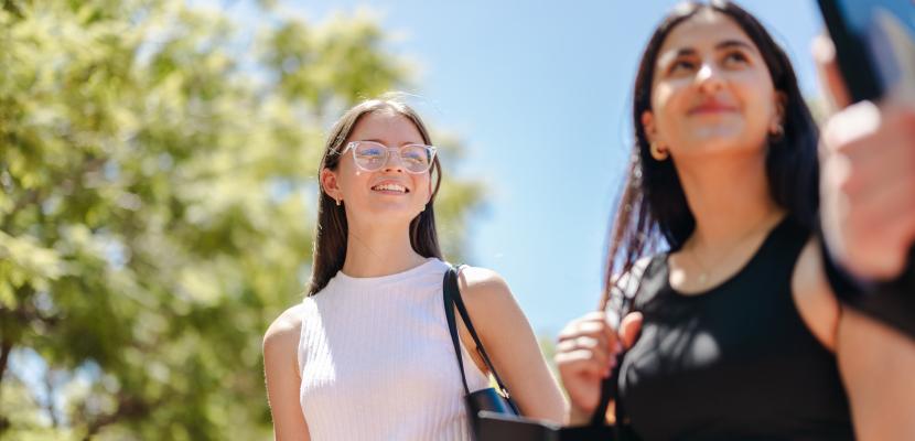 Two young women are smiling as they walk on a sunny day. 