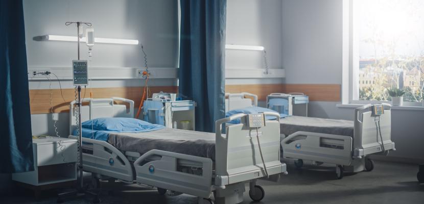 Two empty hospital beds with a curtain between them and lights above them