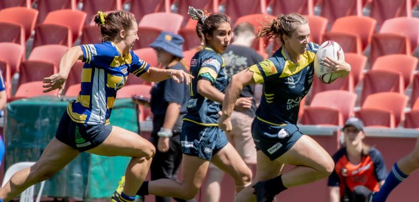 Women's rugby player running past an opponent to score a try.