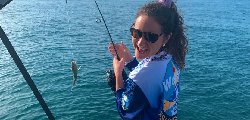 Occupational Therapy student Chloe Calder reeling in a small fish on a boat. 