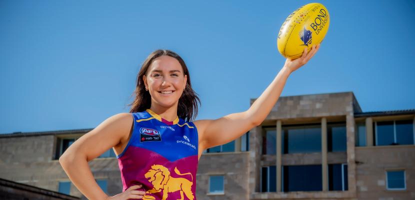 Womens AFL star Mikayla Pauga holding an Aussie rules football in the air in front of the Arch.