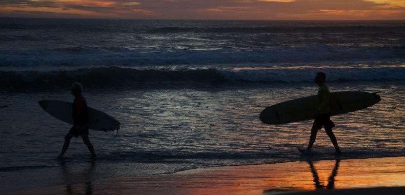 surfers on the beach at sunset