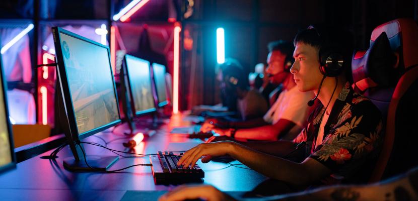 A row of people are looking at screens in a dark room, playing esports. 