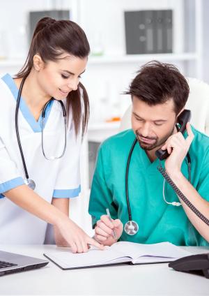 Two doctors are looking at paperwork on a desk, one of them is also on the phone