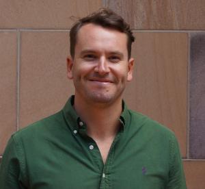 Man in a green shirt standing in front of a wall smiling
