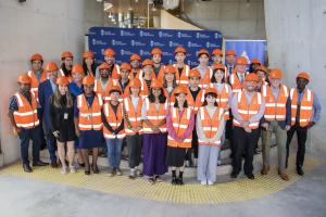 A group of people are wearing hard hats and high-visibility clothing, standing in front of a wall of Bond University logos.