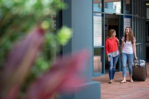 Two students walk through the Bond campus wheeling a suitcase